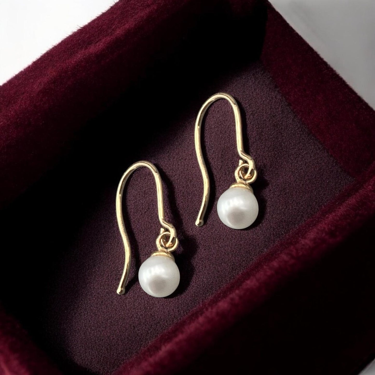 Elegant 14k yellow gold drop earrings featuring round white pearls and a minimalist polished hook design.