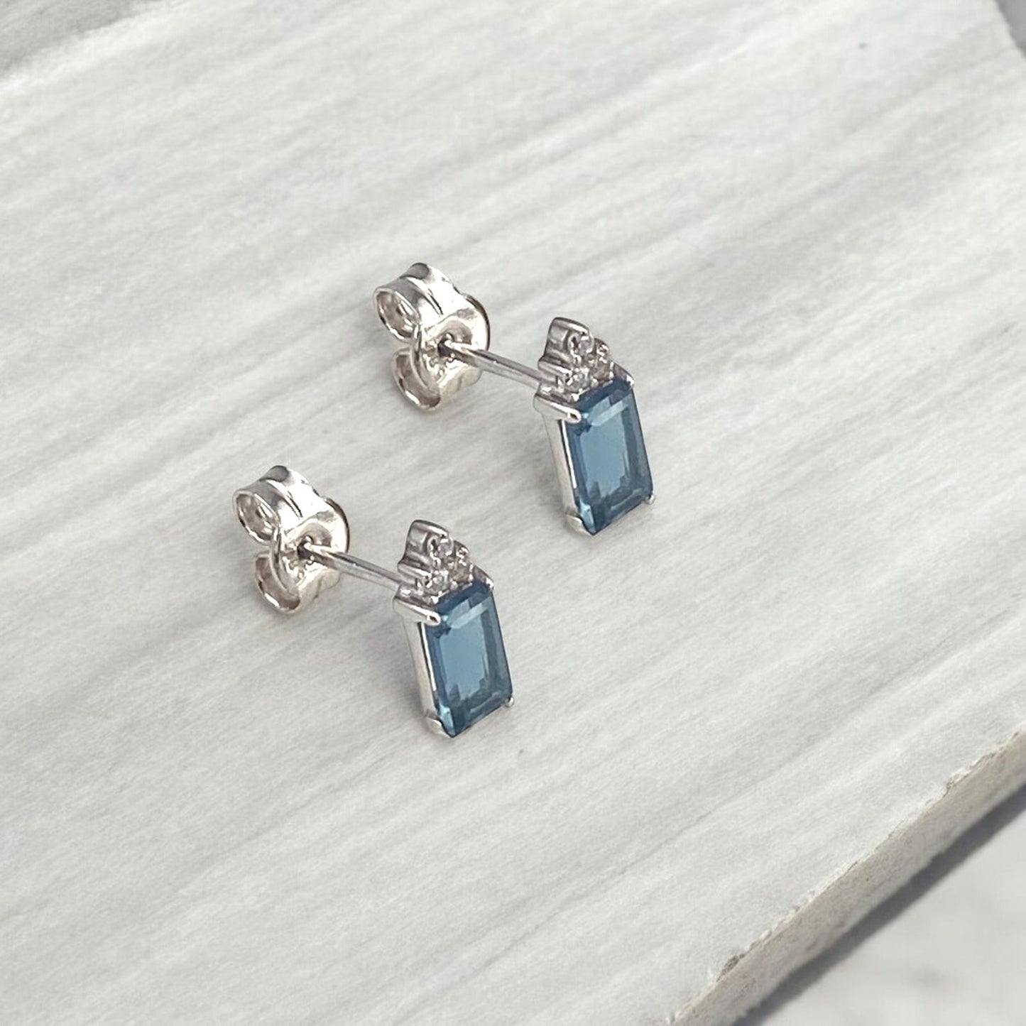 Elegant 14k white gold stud earrings featuring a rectangular blue center stone accented with sparkling diamonds.