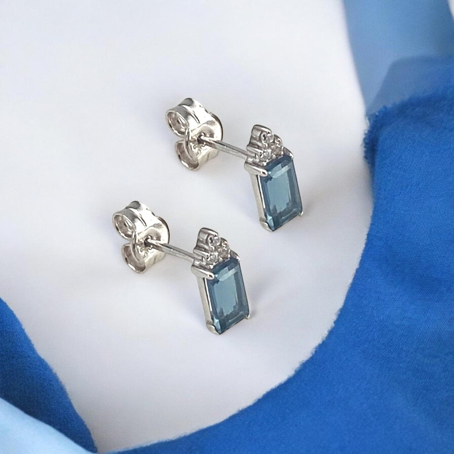 Elegant 14k white gold stud earrings featuring a rectangular blue center stone accented with sparkling diamonds.