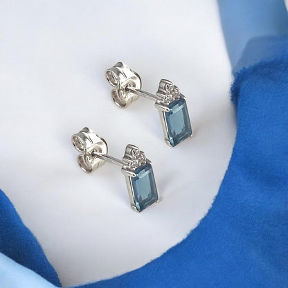 Elegant 14k white gold stud earrings featuring a rectangular blue center stone accented with sparkling diamonds.
