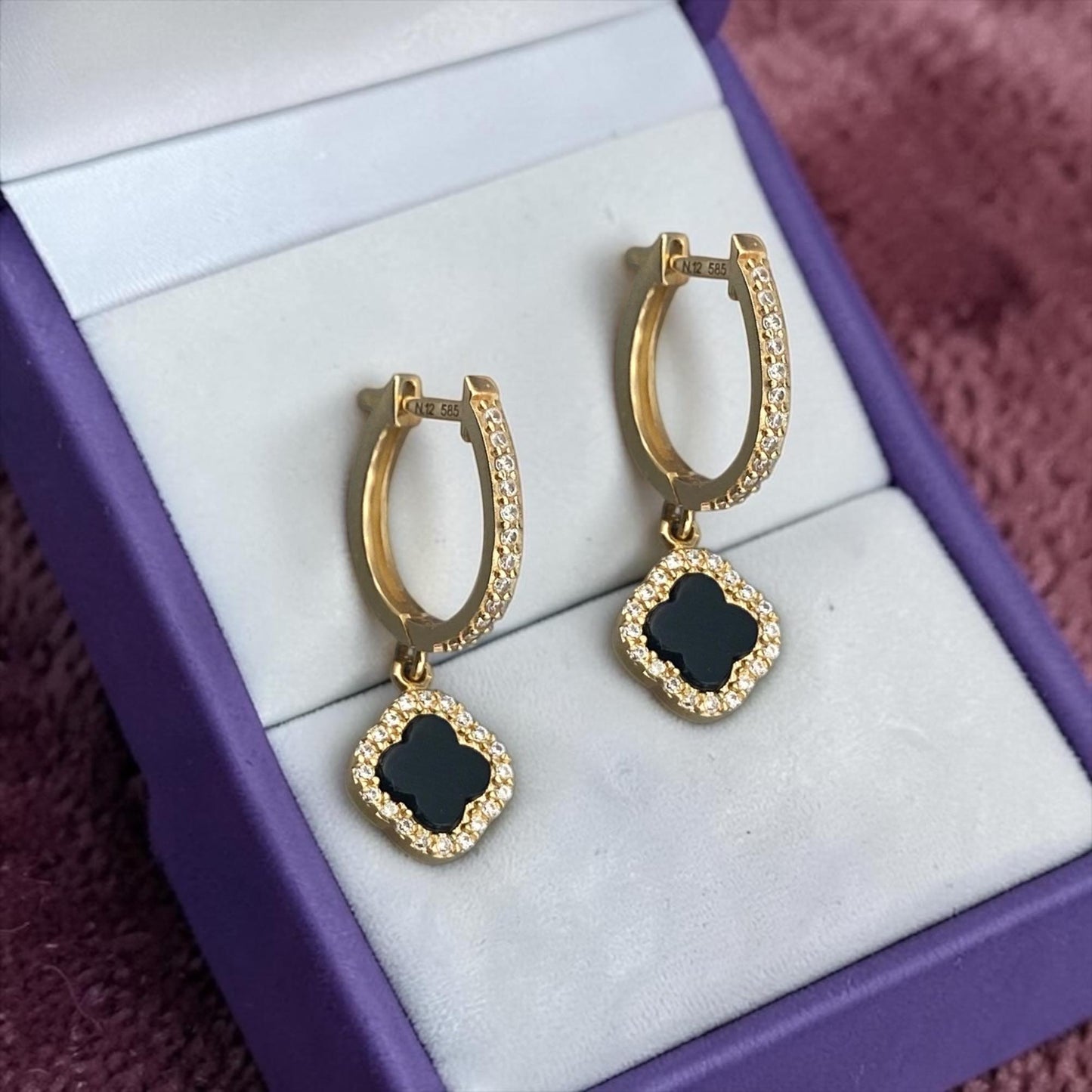 Elegant 14k yellow gold hoop earrings featuring black clover charms with sparkling crystal accents.