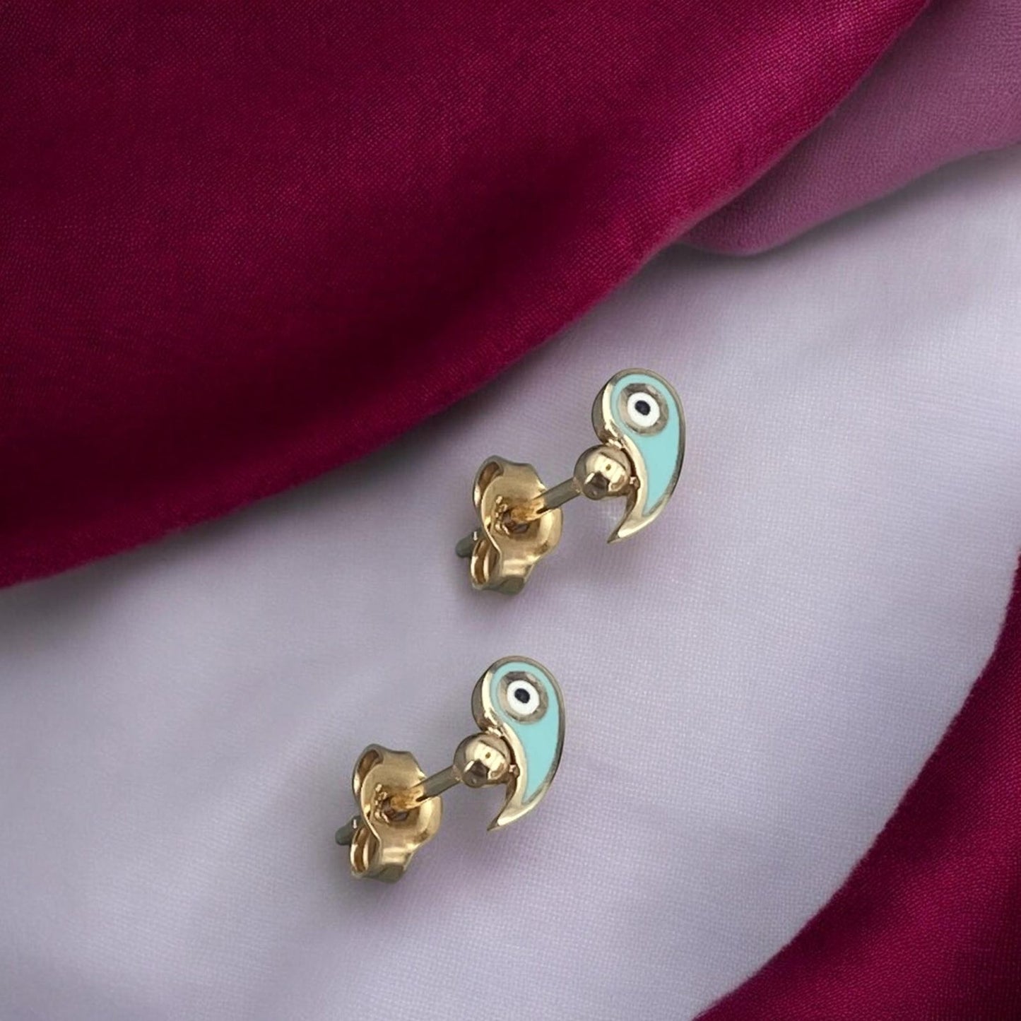 Delicate 14k yellow gold stud earrings featuring a protective evil eye motif accented with vibrant light blue enamel.