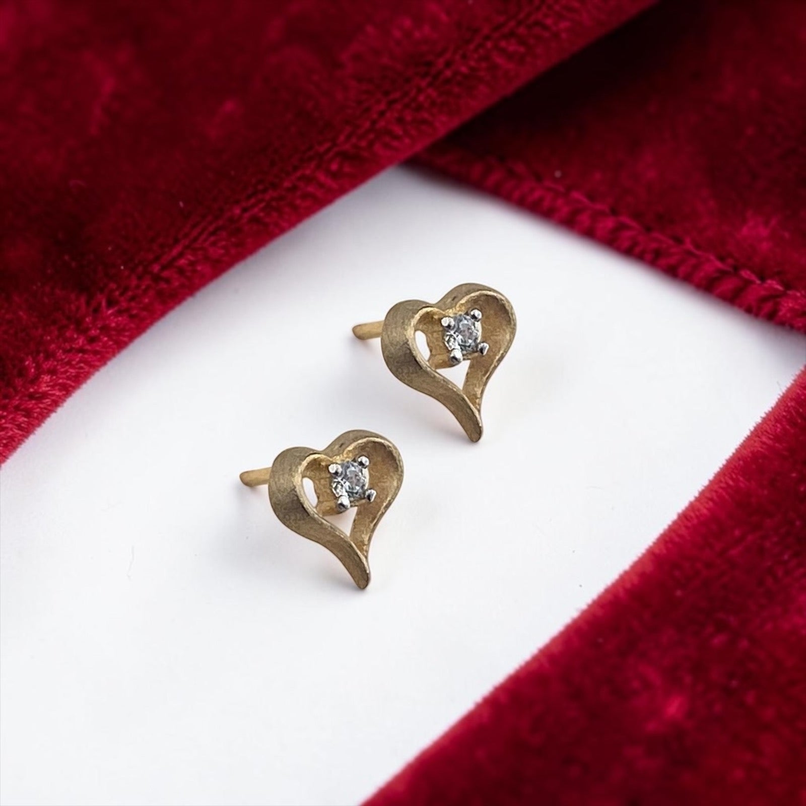 Elegant 14k yellow gold stud earrings featuring a delicate heart design with a sparkling central cubic zirconia stone.