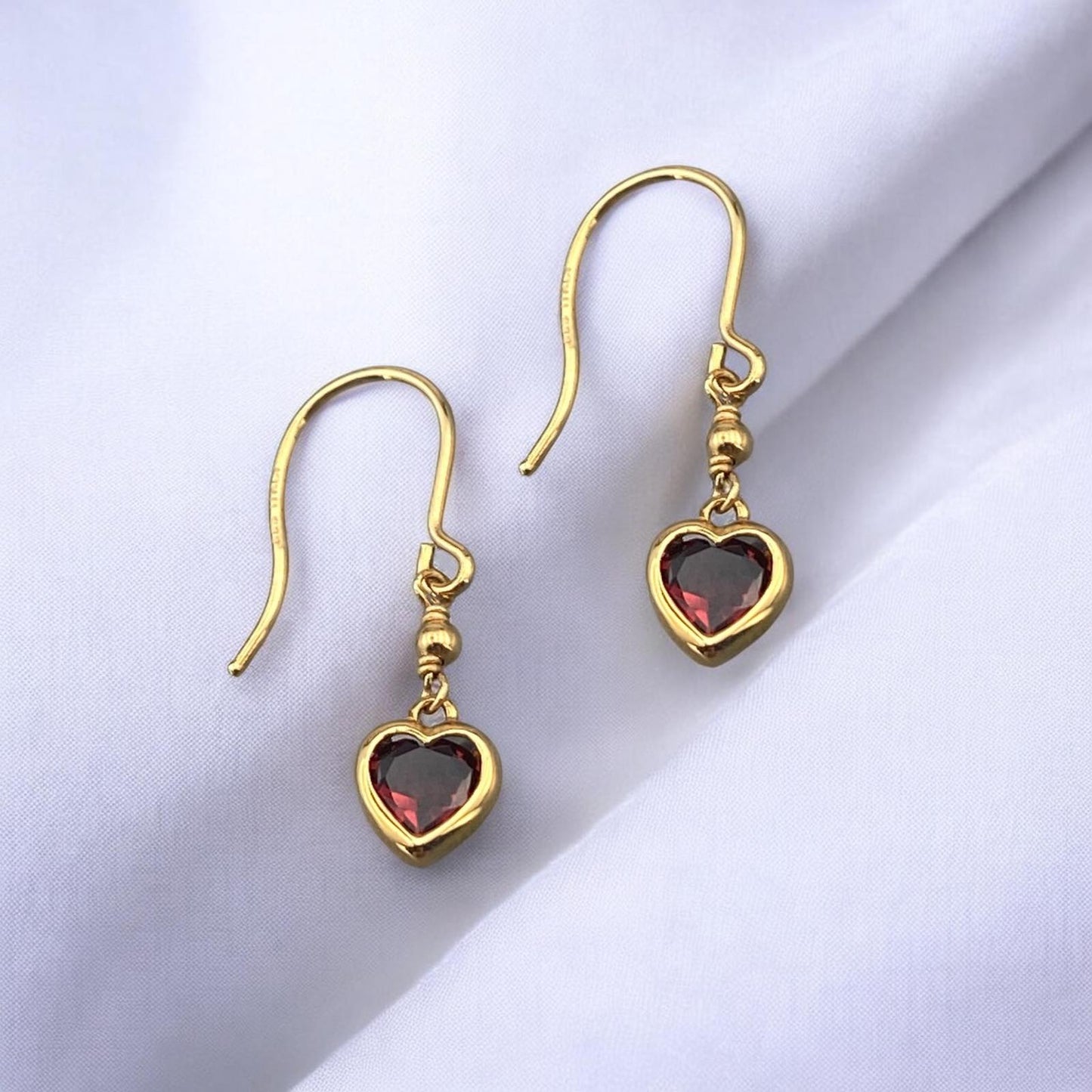 Elegant 14k yellow gold drop earrings featuring a delicate heart-shaped red garnet stone and a secure hook fastening.