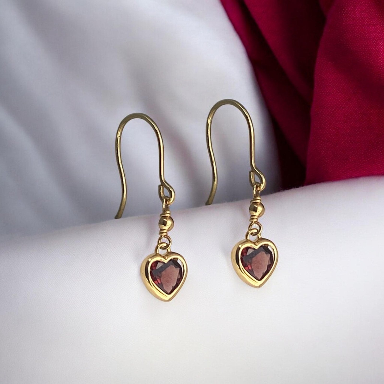 Elegant 14k yellow gold drop earrings featuring a delicate heart-shaped red garnet stone and a secure hook fastening.