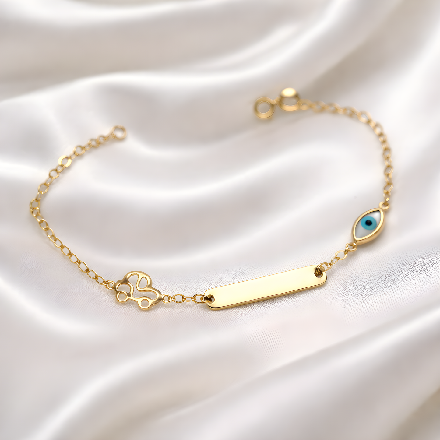 Gold bracelet with a blue eye charm and a gold car on a white satin background