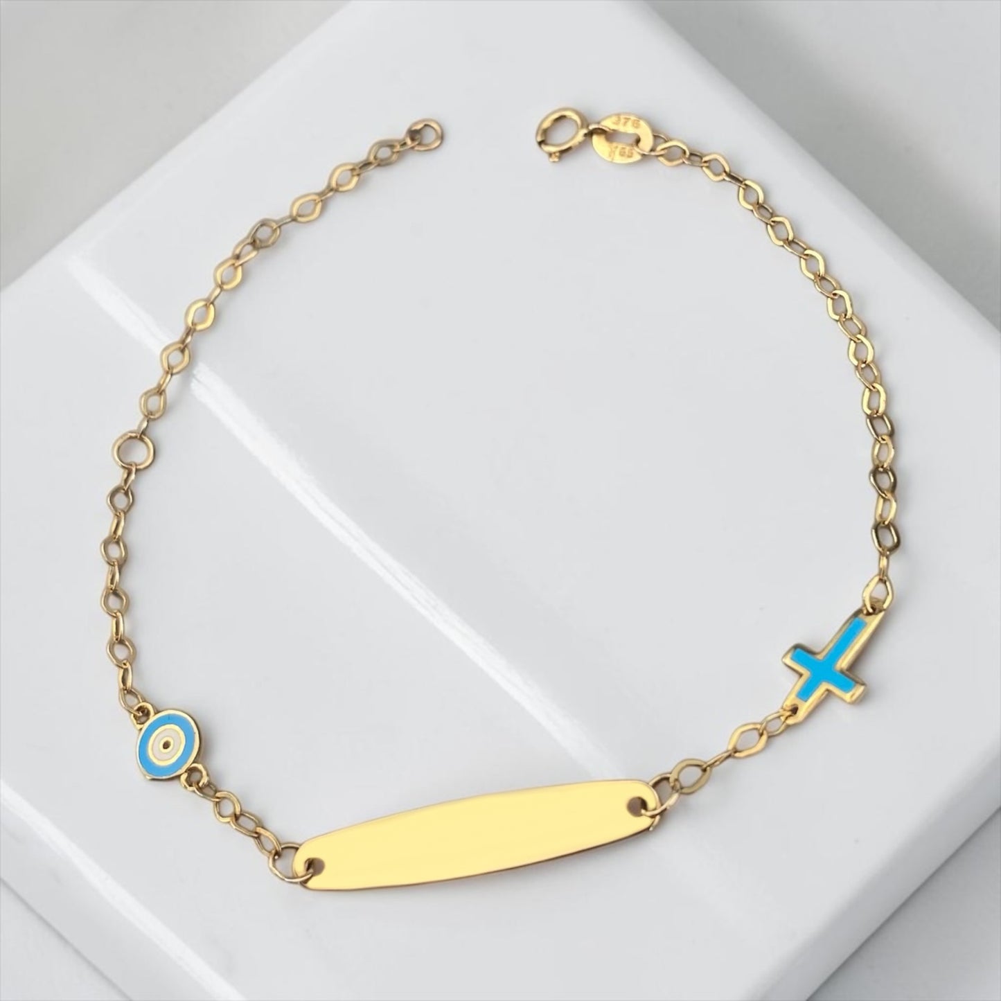 Children's 9k yellow gold ID bracelet featuring an blue eye charm and a cross charm, delicate baby jewelry.